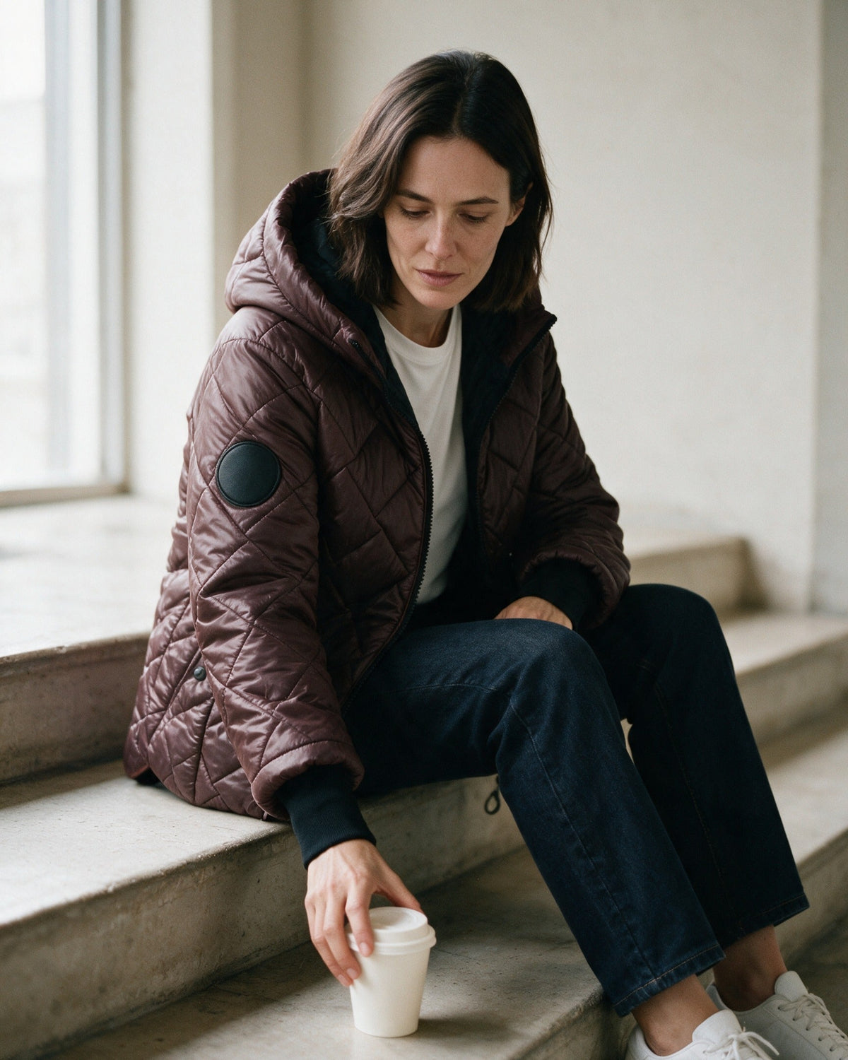 Ainsley puffer jacket in Chocolate, worn sitting on a step